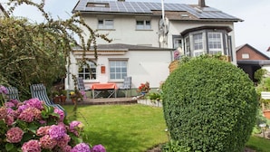 A house with solar panels, a well-maintained garden, and a patio with chairs. - Attractive Apartment in Bettenfeld With Garden (Bettenfeld)