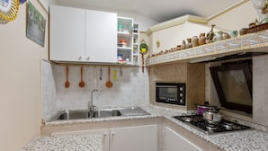 Une cuisine compacte avec des meubles blancs, un four à micro-ondes encastré, une cuisinière à gaz et un évier.