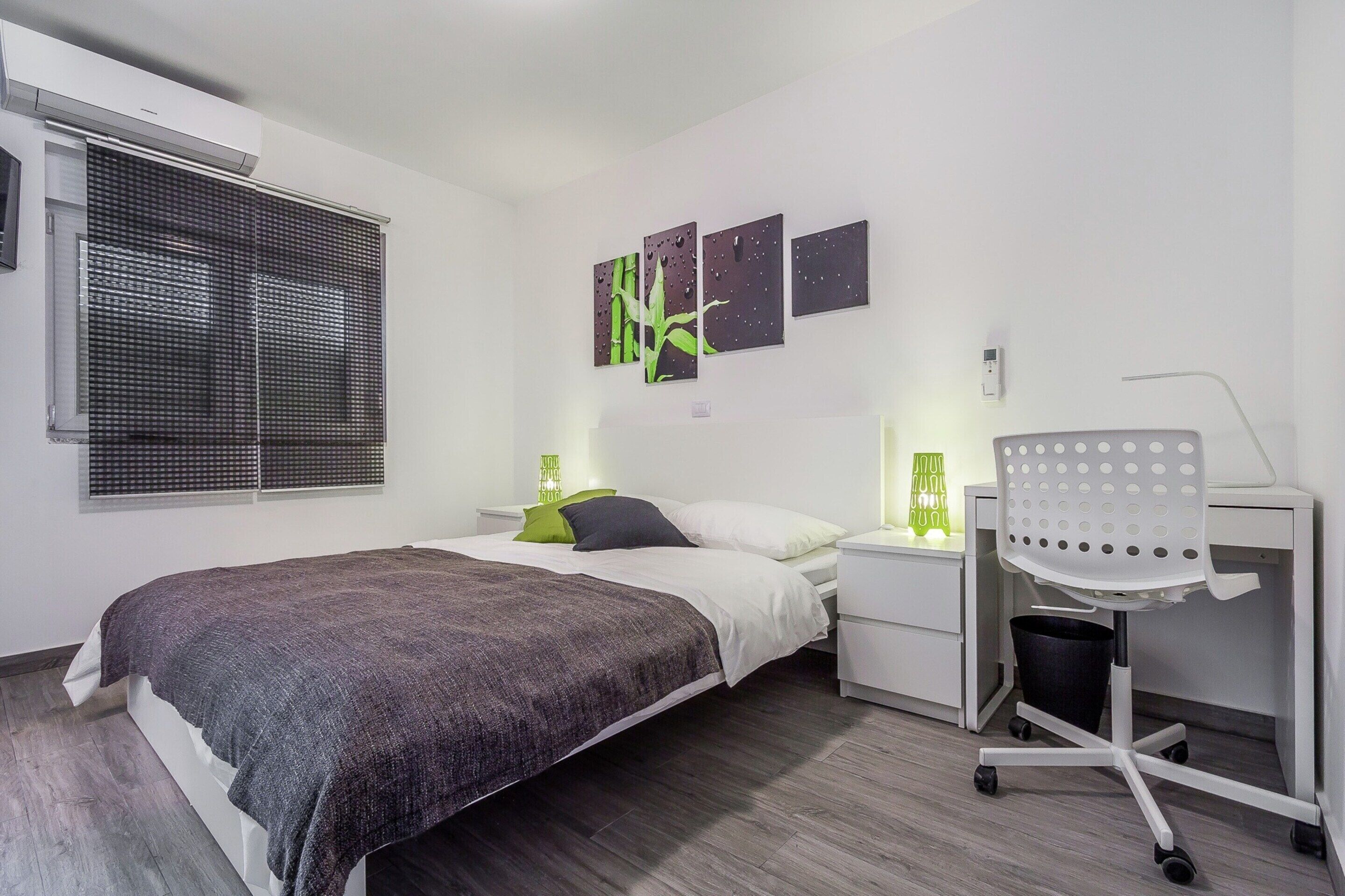 A modern bedroom with a bed, bedside tables, a desk with a chair, and wall art.