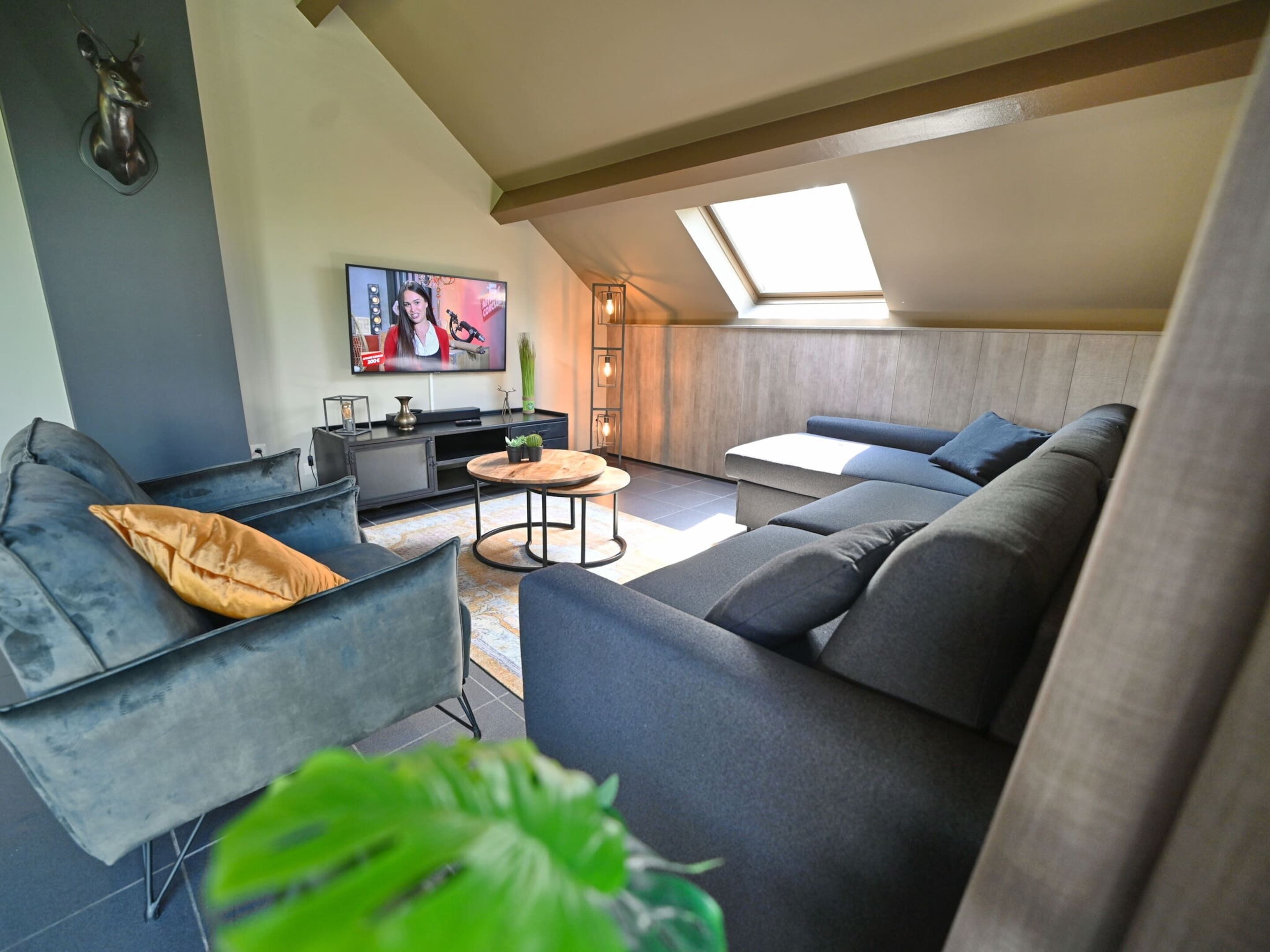 A modern loft-style living room with a large sofa, a coffee table, and a TV mounted on the wall.