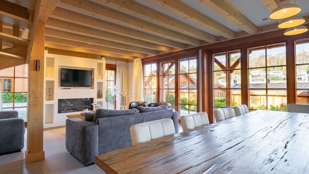 Un vaste espace de vie comprenant une grande table à manger en bois, des canapés gris et un téléviseur fixé au mur.