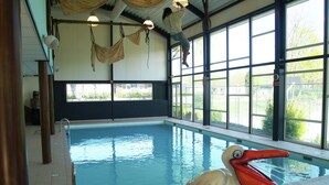 Ein Hallenbad mit einem großen Fenster, einem Rettungsschwimmerstand und einer dekorativen Vogelstatue.