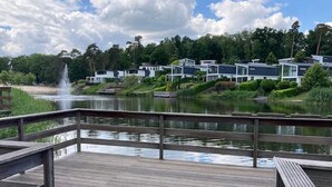 Une terrasse en bois donnant sur un lac, avec des bâtiments modernes en arrière-plan.