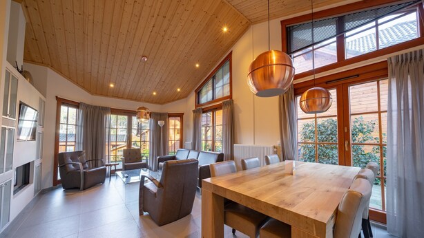 Un vaste espace de vie doté d’un plafond en bois, de grandes fenêtres et d’une table centrale en bois.