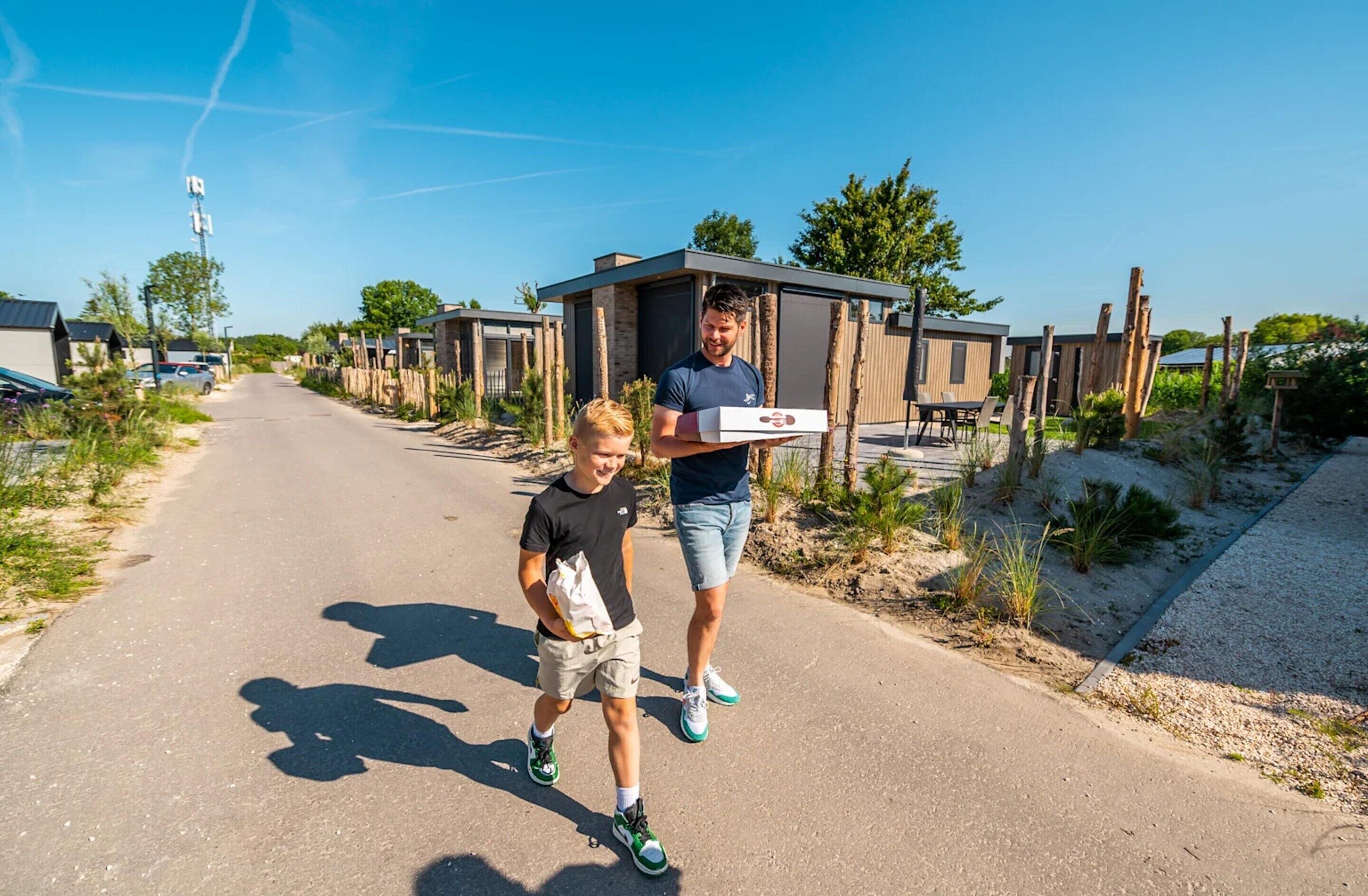 A person carrying a pizza box on a road with modern houses in the background.