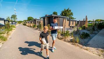 A person carrying a pizza box on a road with modern houses in the background.