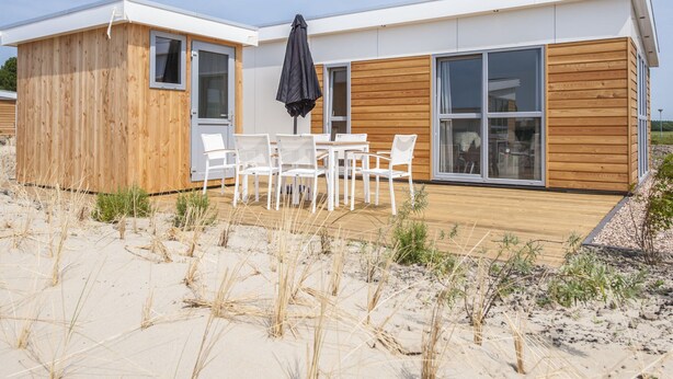 A modern beach house with a wooden deck, white outdoor furniture, and large sliding glass doors. - Comfortable Chalet With Combi Microwave, Near Rockanje (Hellevoetsluis)