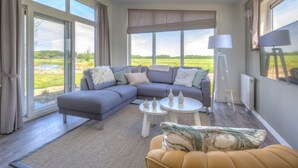 A modern living room with a sectional sofa, a round coffee table, and a view of a green field through large windows. - Comfortable Chalet With Combi Microwave, Near Rockanje (Hellevoetsluis)