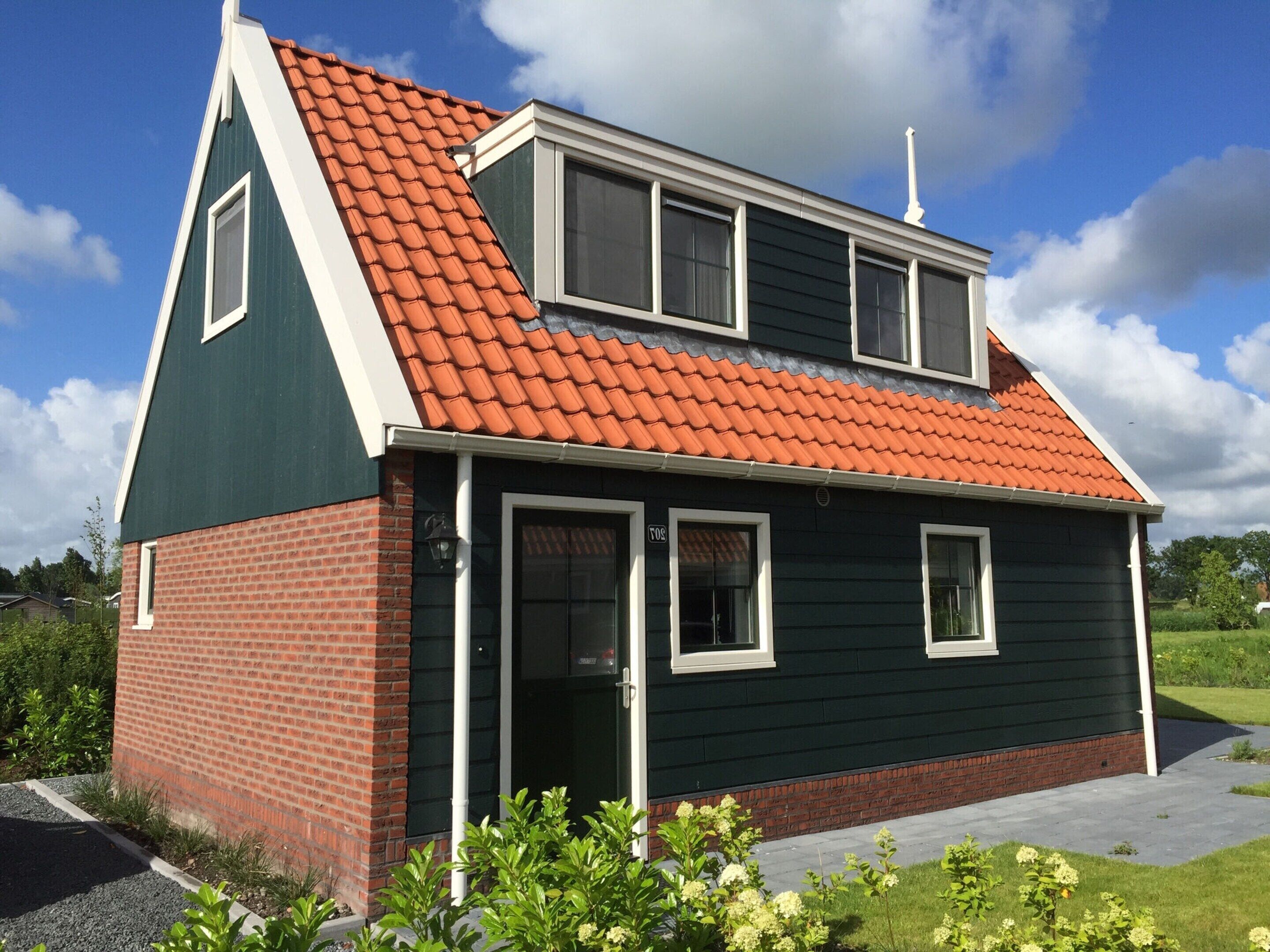 Een twee verdiepingen tellend huis met een rode dakbedekking, een gevel van baksteen beneden en een donkergroen gedeelte boven.