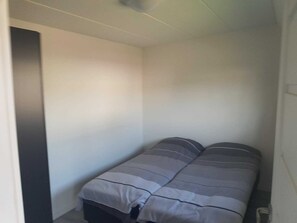 A narrow room with a bed against the wall, a door on one side, and a small window on the opposite wall. - Chalet With Dishwasher in the Green Kempen (Mol)