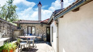 A stone patio with a table and chairs, a potted plant, and a view of a building with chimneys. - Farmhouse in Casoli Near Ski Slopes (Bagni di Lucca)