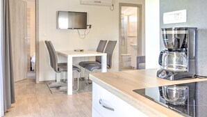 Una cocina moderna con cafetera, un comedor con sillas y un televisor montado en la pared.