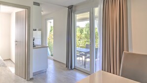 Una habitación de hotel moderna con zona de comedor, kitchenette y puerta corrediza de vidrio que da a un patio exterior.