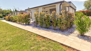Una casa moderna de dos plantas con un porche cubierto, rodeada de jardines cuidados y un sendero pavimentado.