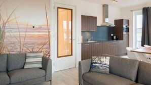 A modern living room with two grey sofas, a round wooden coffee table, and a large window with a view of a beach. - Modern Apartment 3 Bath Rooms, Close to Lake Veere (Kamperland)