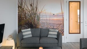 A modern living room with a grey sofa, a wooden coffee table, and a wall mural of tall grasses and a sunset. - Modern Apartment 3 Bath Rooms, Close to Lake Veere (Kamperland)