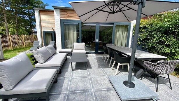 An outdoor patio with a sofa, chairs, a table, and an umbrella. - Holiday Home Nieuwvliet Near Beach (Nieuwvliet)