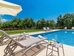A swimming pool with lounge chairs and a table, surrounded by greenery. - Luxurious Villa in Butkovici with Pool & Hot Tub (Svetvincenat)