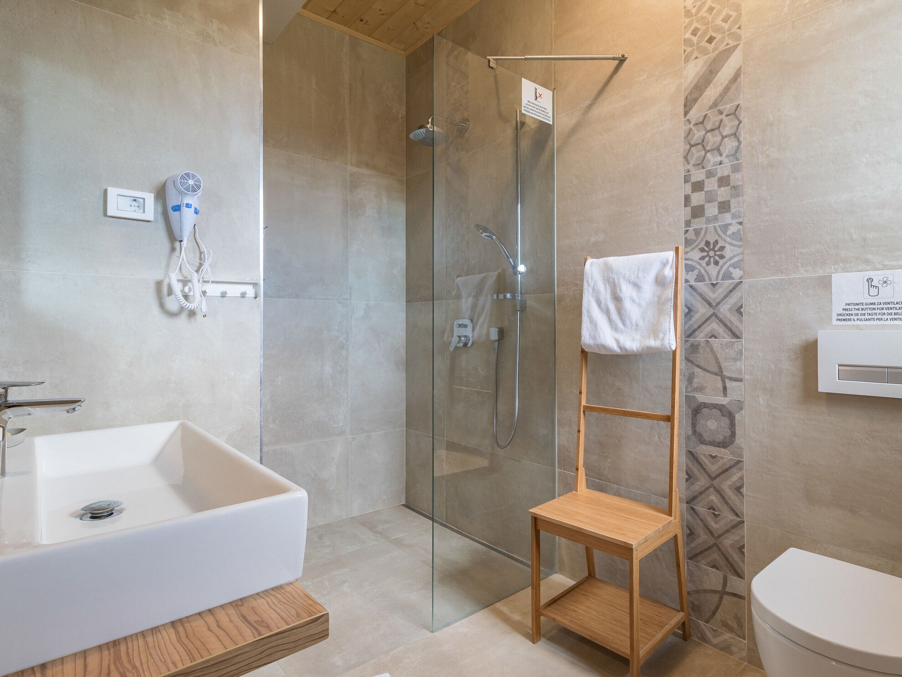 Une salle de bain moderne avec une douche à parois de verre, un tabouret en bois, une baignoire blanche et des toilettes.