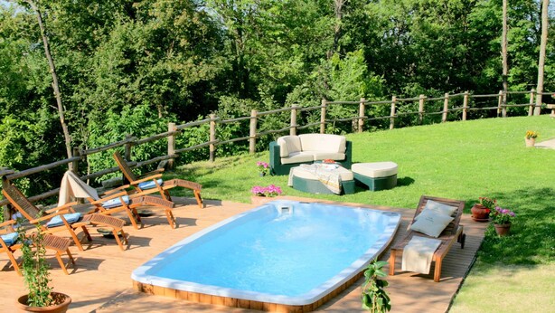 Um quintal com hidromassagem, cadeiras de descanso e um deck de madeira.
