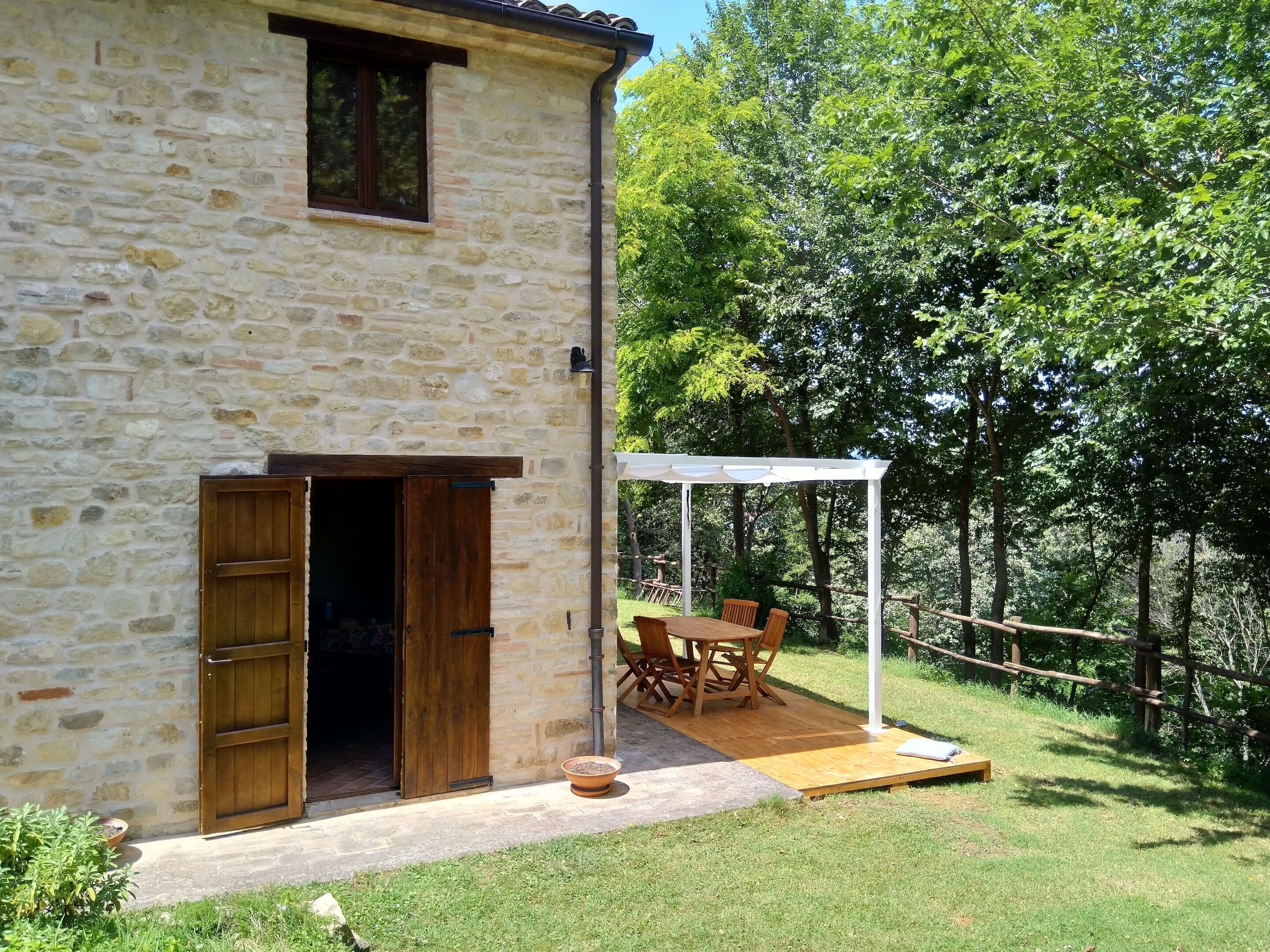 Ein Steinhaus mit einer Holztür und einer überdachten Veranda mit Tisch und Stühlen.