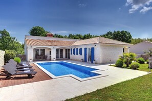 Ein modernes Haus mit Schwimmbad, einer Terrasse mit Liegestühlen und einem gepflegten Garten.