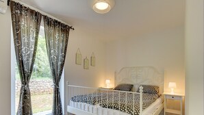 A bedroom with a white metal bed frame, two bedside tables with lamps, and a window with floral curtains. - Comfortable Villa With Private Swimming Pool, Table Football, Near Labin (Sveta Nedelja)
