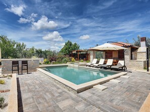 A pool area with lounge chairs, a stone wall, and a pergola with an umbrella. - Holiday Home Medulin With Pool Near Beach (Medulin)