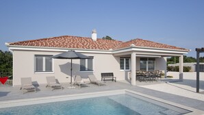Ein modernes Haus mit Swimmingpool, Sitzgelegenheiten im Freien und einer überdachten Terrasse.