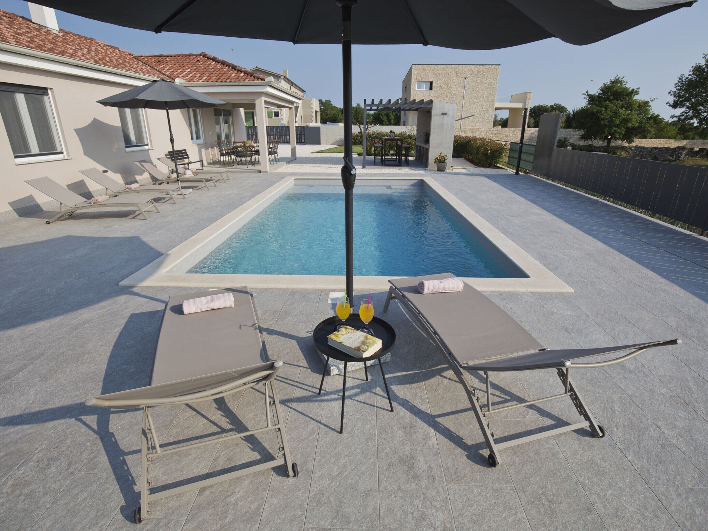 A poolside area with lounge chairs, a table with drinks, and umbrellas.
