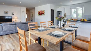 Eine moderne Küche mit Essbereich, ein graues Sofa und ein Fernseher im Wohnzimmer.