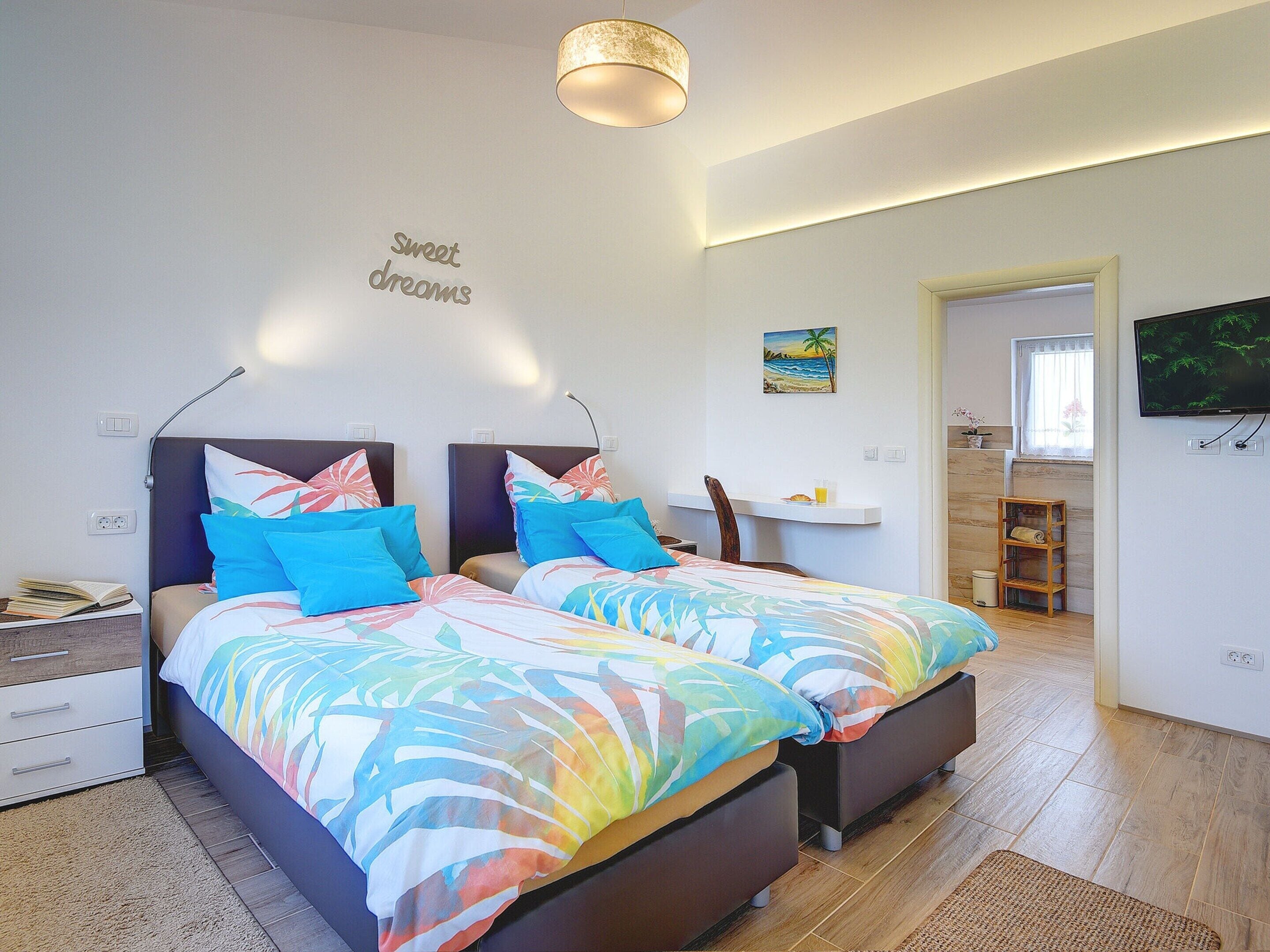 A modern bedroom with two beds, a small desk, and a TV.