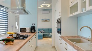 Cocina estrecha con encimera de madera, estufa, microondas y lavamanos. Se observa un sofá azul al fondo.