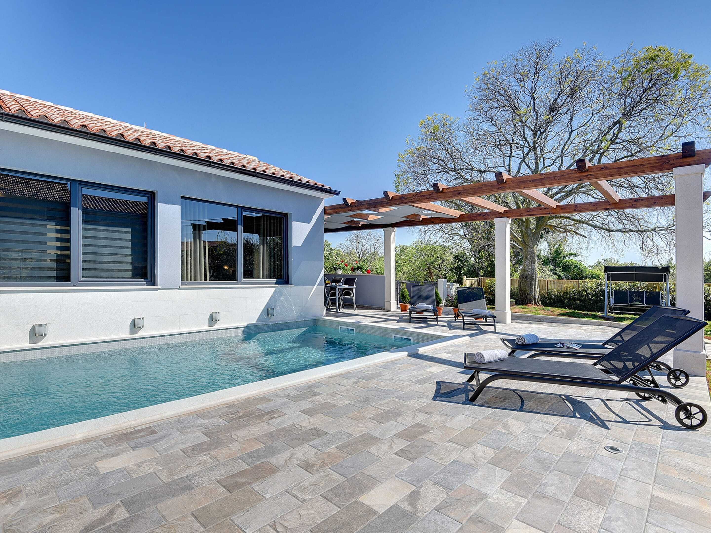 Una casa moderna con piscina, mobiliario exterior y una pérgola.
