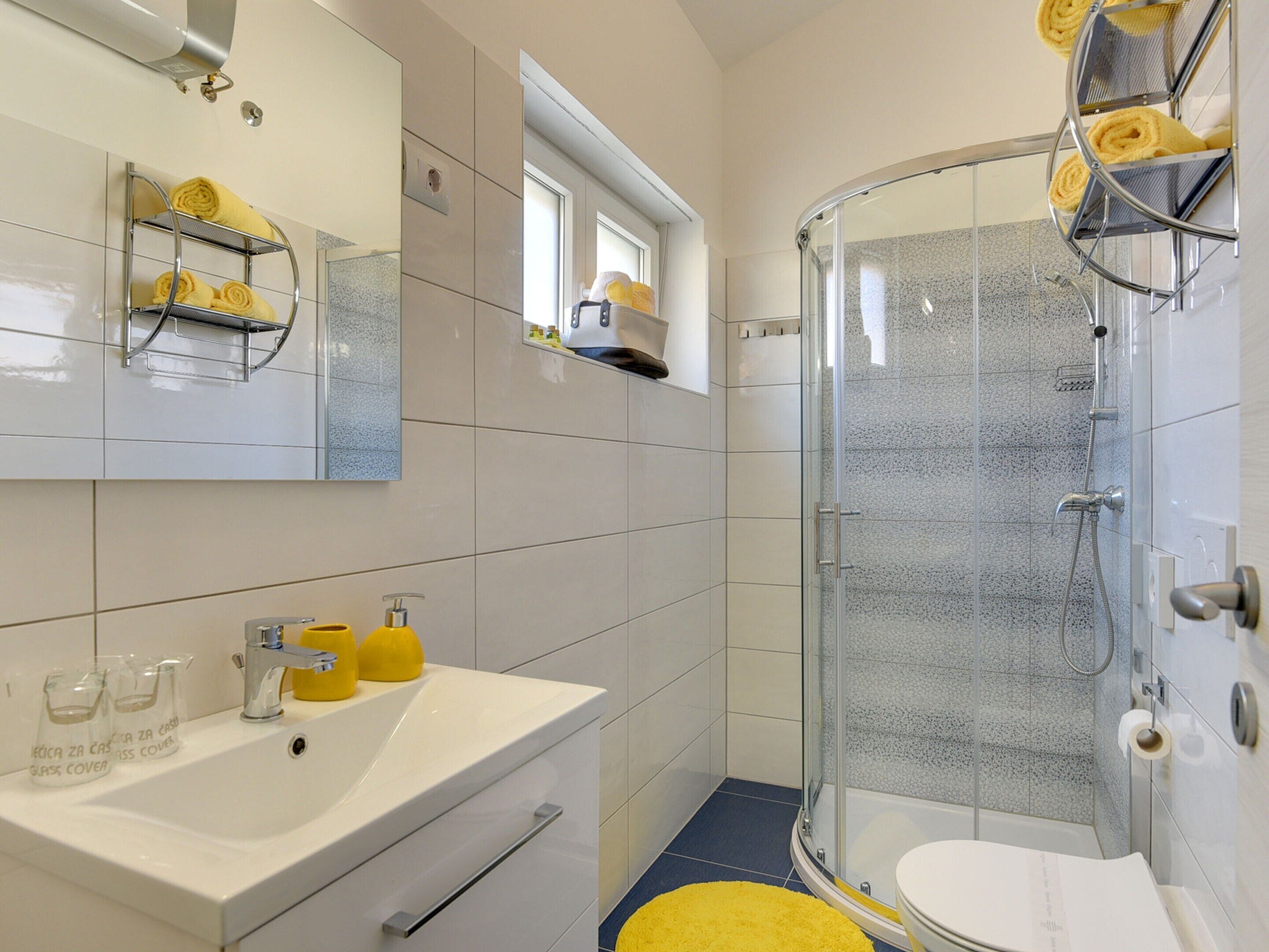 Une salle de bain moderne avec une douche en verre, un lavabo blanc avec un savon jaune, et un miroir au-dessus.