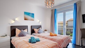 Ein Hotelzimmer mit zwei Betten, einem großen Fenster mit Vorhängen, einem Bild an der Wand und einer Deckenleuchte.