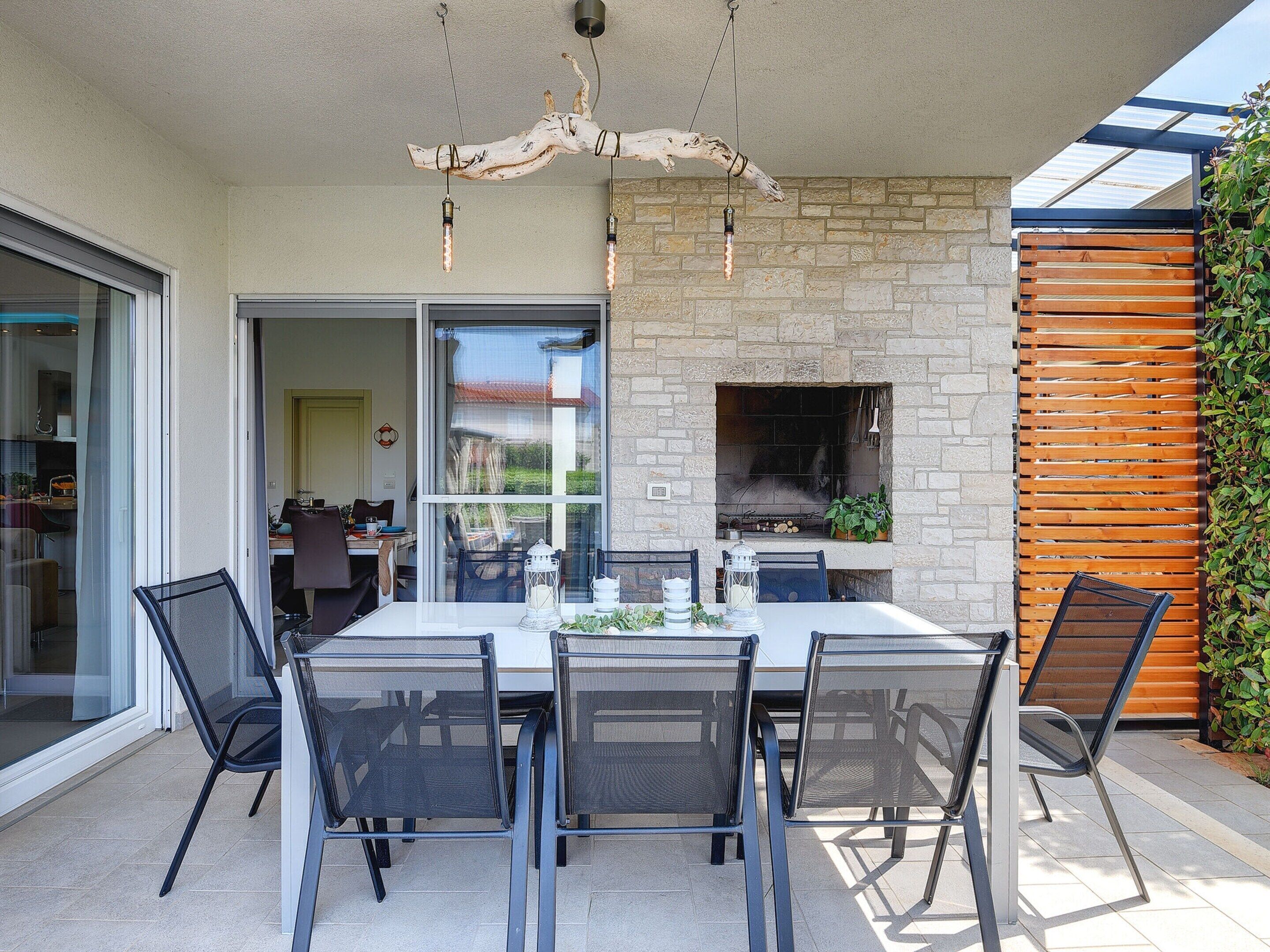 An outdoor dining area with a stone fireplace, a grill, and a view of the backyard.