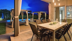 Eine Terrass mit Esstisch und Stühlen, einem überdachten Sitzbereich und einem Pool im Hintergrund.