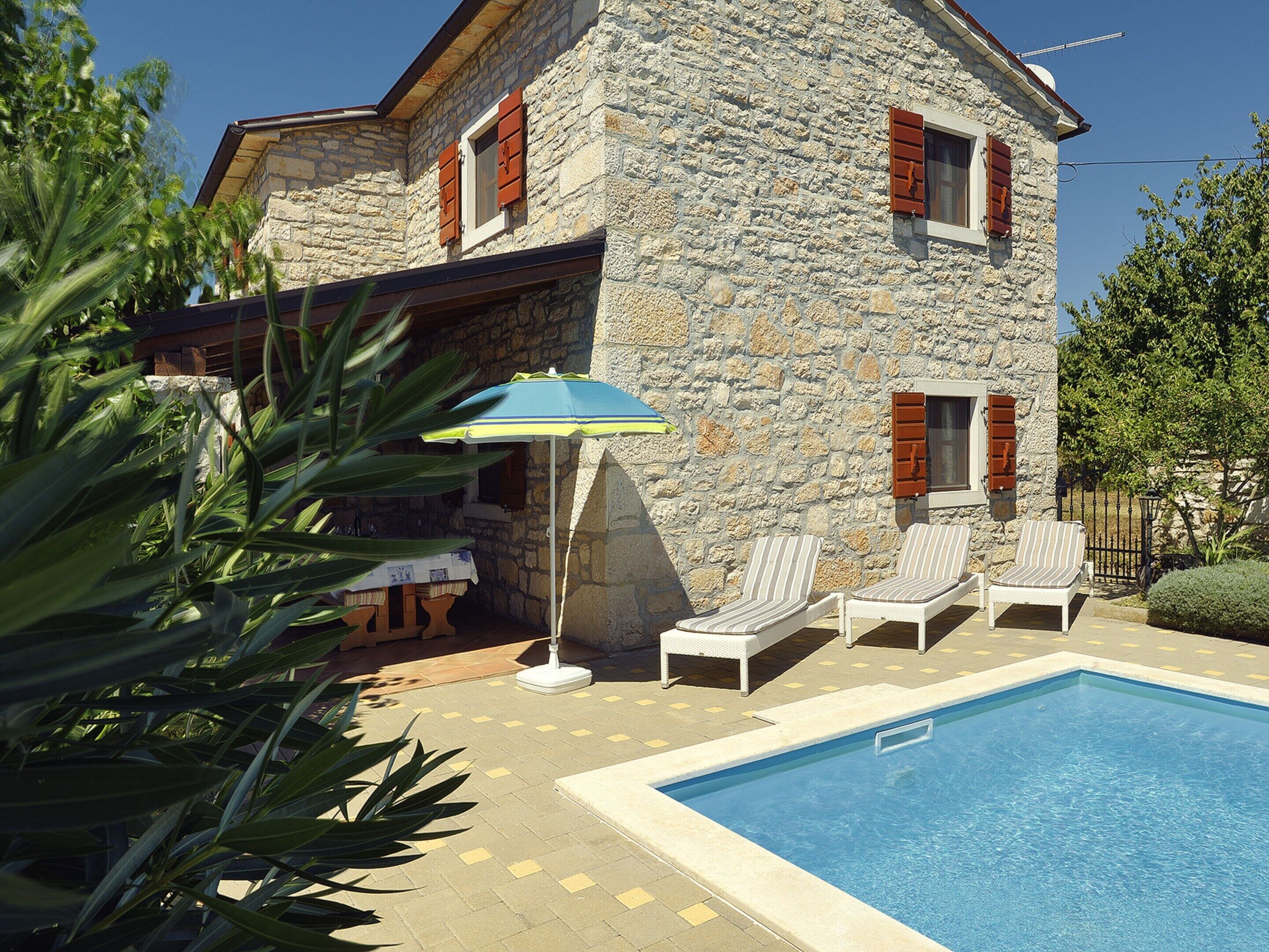 A stone building with a swimming pool, outdoor seating, and a table with a tablecloth.