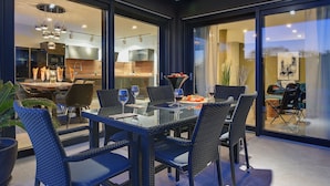 A modern dining area with a glass table, wicker chairs, and a view of the kitchen and living area through large glass doors. - Holiday Home in Rovinj With Pool and Sauna (Rovinj)