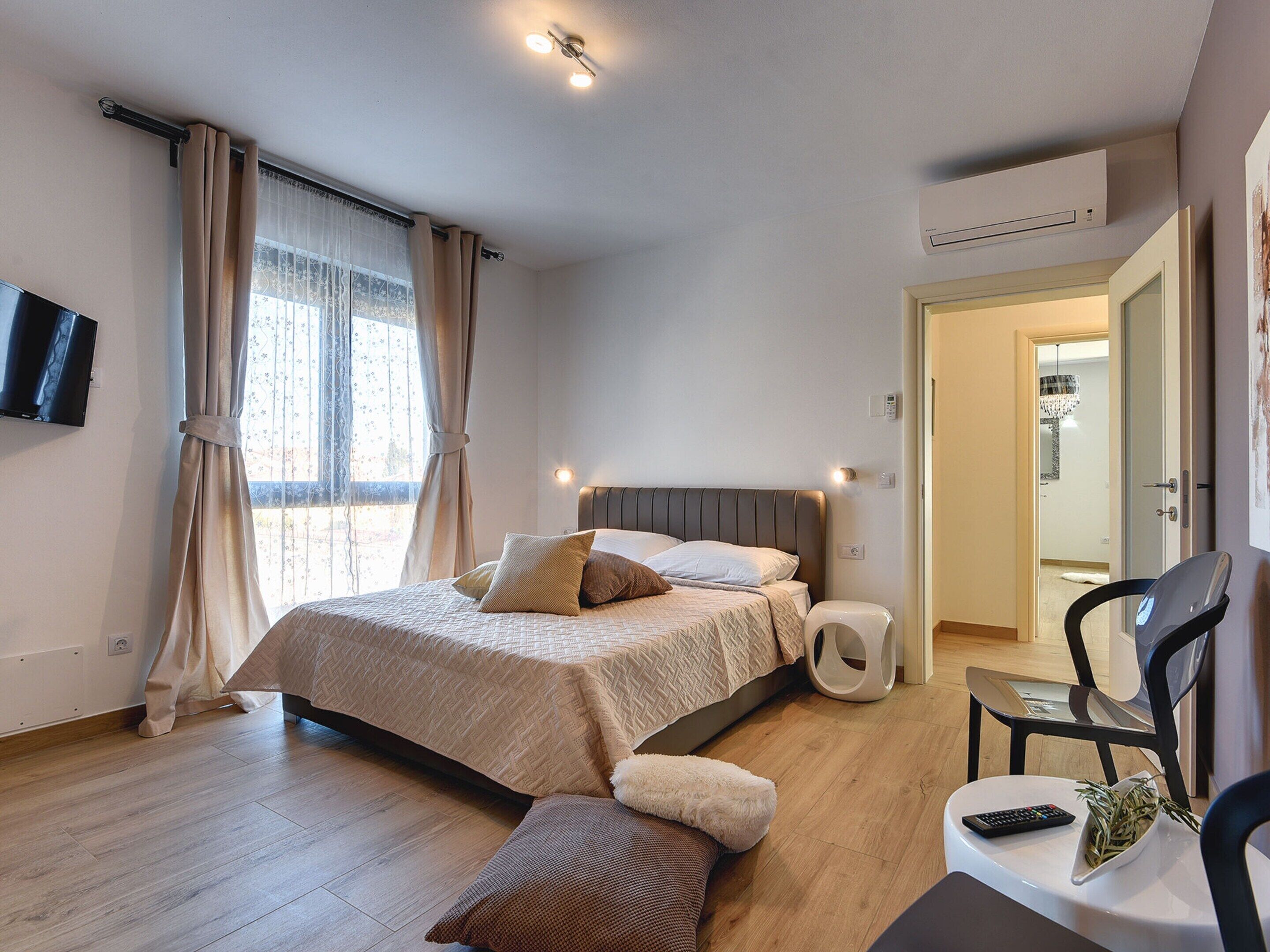 A modern hotel room with a bed, bedside table, chair, and a TV mounted on the wall.