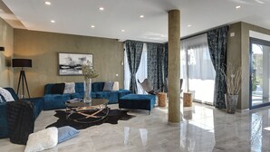 A modern living room with a blue sofa, a coffee table, and a large window with curtains. - Holiday Home in Rovinj With Pool and Sauna (Rovinj)