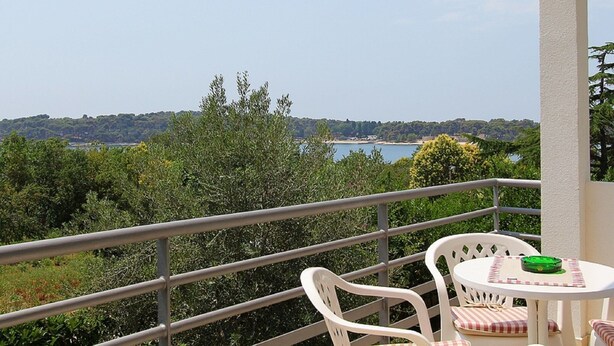 En balkon med udsigt over et sølandskab og bakker, med to hvide plastikstole og et lille rundt bord med en grøn genstand på.