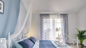 Une chambre à coucher comprenant un lit, une table de chevet, une chaise, une plante en pot et une vue sur l’extérieur.