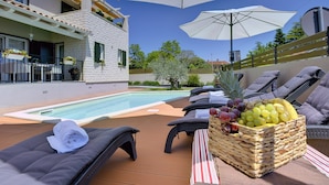 Un espace aménagé au bord de la piscine, avec des chaises longues, un panier en osier rempli de fruits et des parasols.