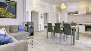 A modern living room with a sofa, a dining table with chairs, a kitchen area with appliances, and a painting on the wall. - Boutique Villa in Peroj With Garden (Vodnjan)