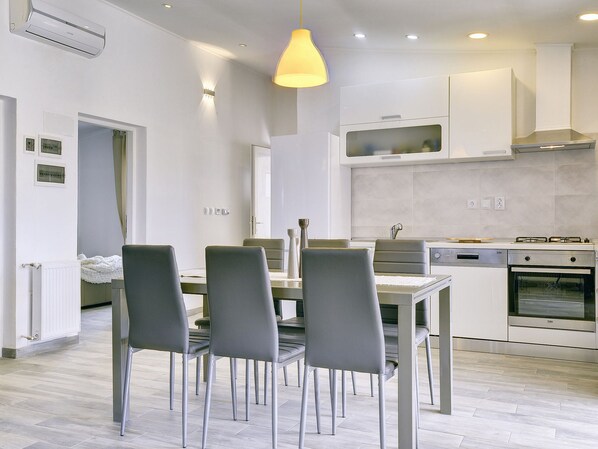 A modern kitchen with white cabinets, a dining table with chairs, and a hanging pendant light. - Villa in Peroj Near the Sea With Terrace (Vodnjan)