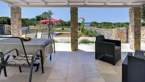 A covered patio with stone pillars, outdoor furniture, and a table set with fruits. - Boutique Villa in Peroj With Garden (Vodnjan)