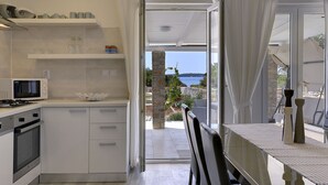 A modern kitchen with white cabinets, a microwave, and a view of the sea through an open door. - Boutique Villa in Peroj With Garden (Vodnjan)