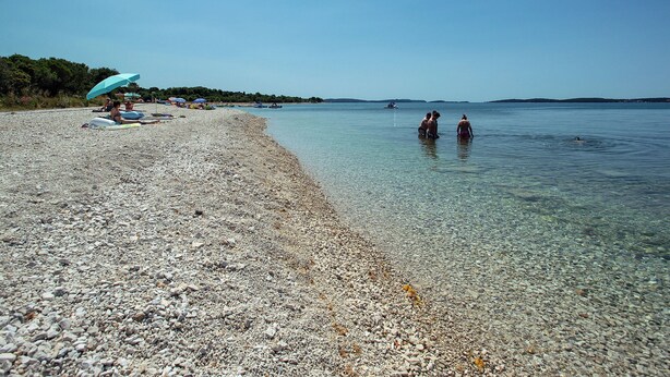 A pebbled beach with clear water, umbrellas, and boats in the distance. - Boutique Villa in Peroj With Garden (Vodnjan)